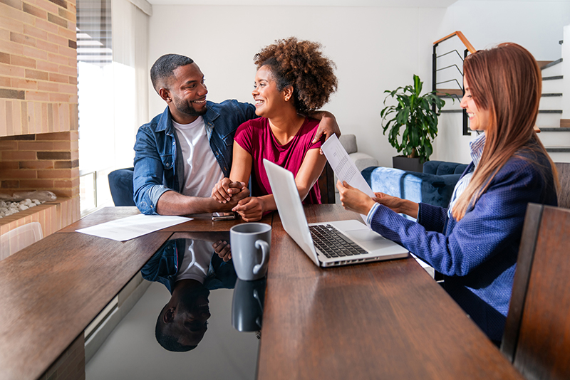 Loving couple looking very excited while buying a house to a real estate agent and sorting the paperwork