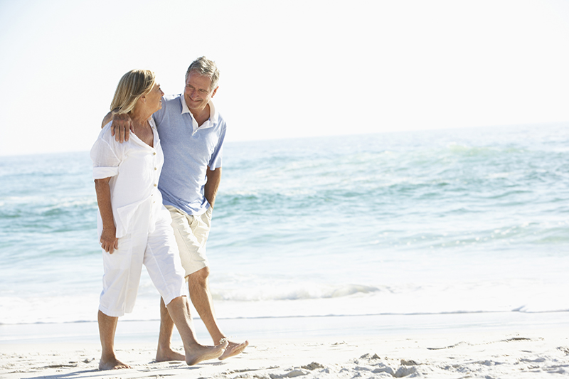 Senior Couple On Holiday Walking Along Beach